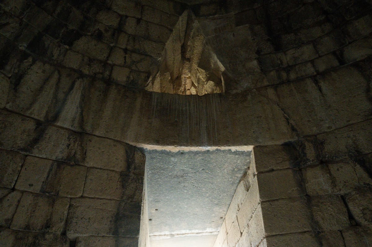 From inside the chamber, looking back at the doorway: the courses of the false dome curve overhead, and the void of the relieving triangle opens above the lintel.