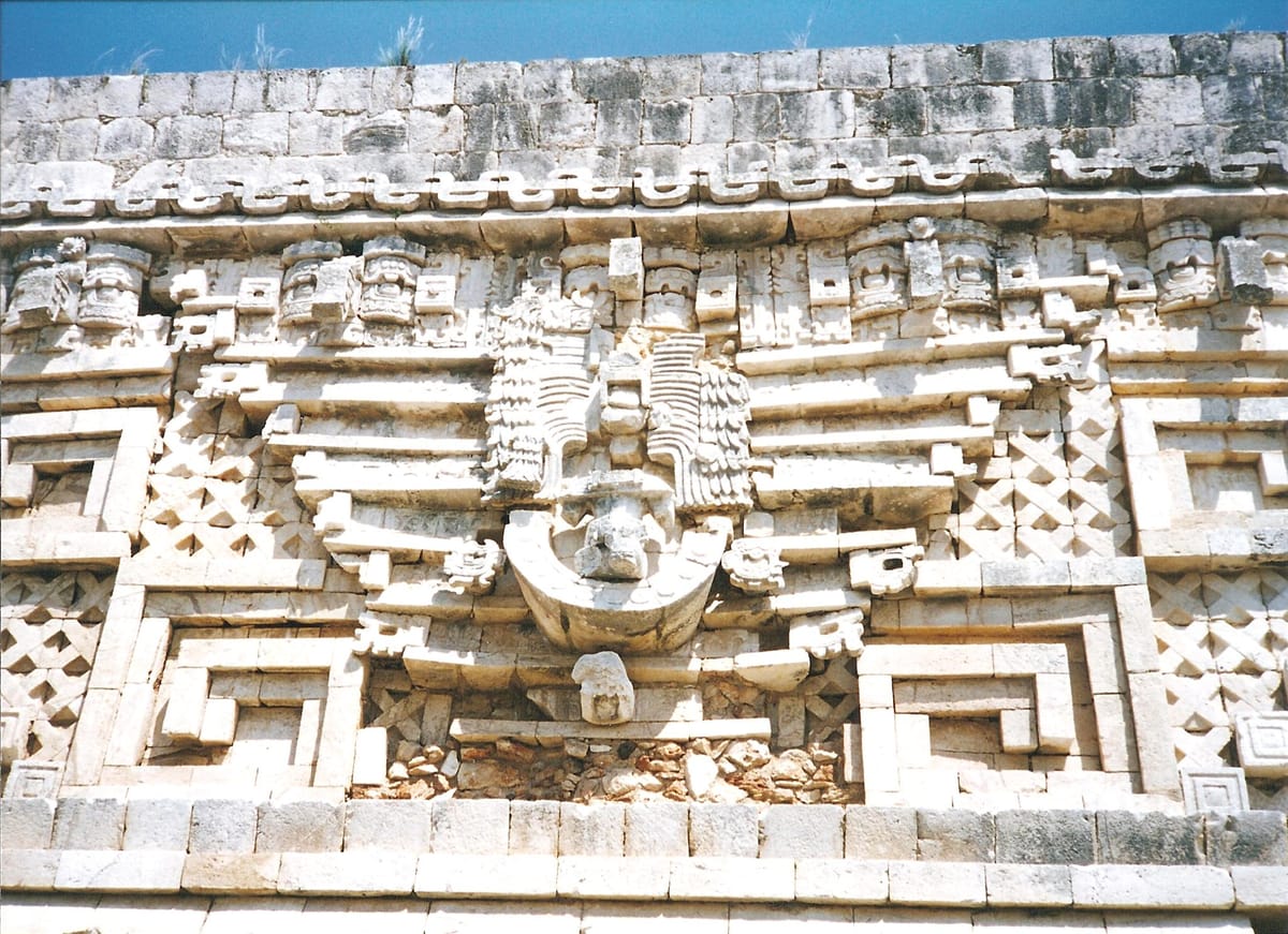 Detail of the Governor's Palace frieze: a hook-nosed Chaac mask built up from dozens of separately carved stones, set among step-frets and lattice panels.