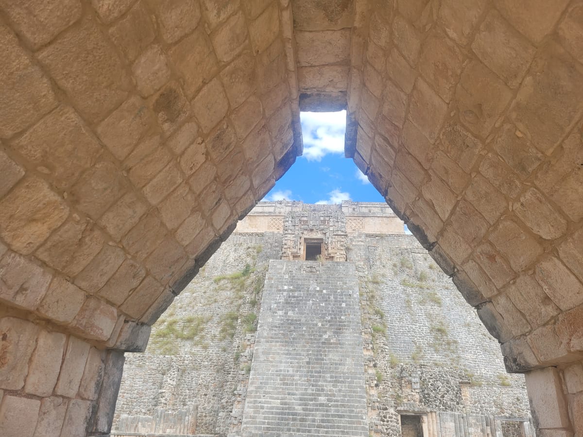 Looking through a Maya corbel arch toward the Pyramid of the Magician: two inward-stepping walls of dressed stone meeting at a narrow capstone.