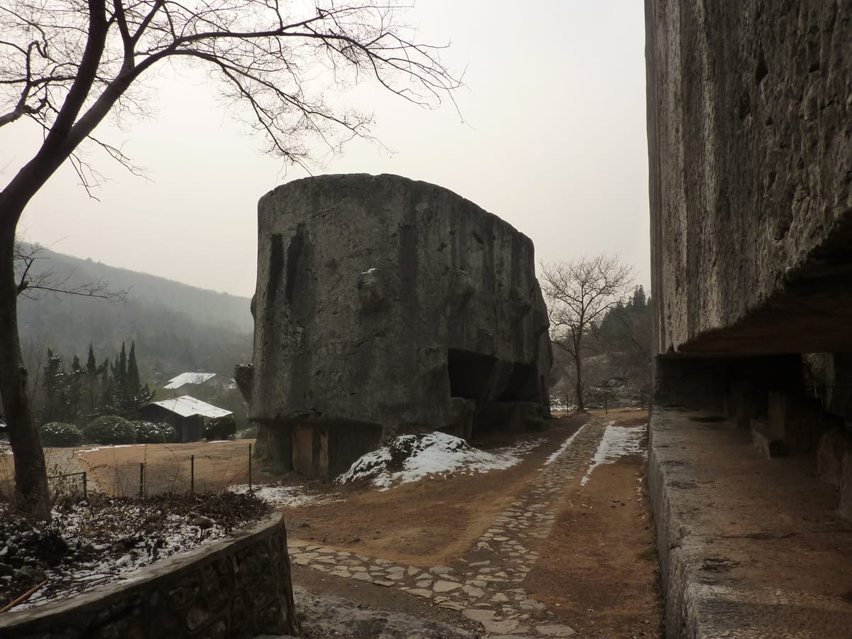 The stele head and stele body lying side by side in the quarry, both largely cut free from the surrounding bedrock but never moved.